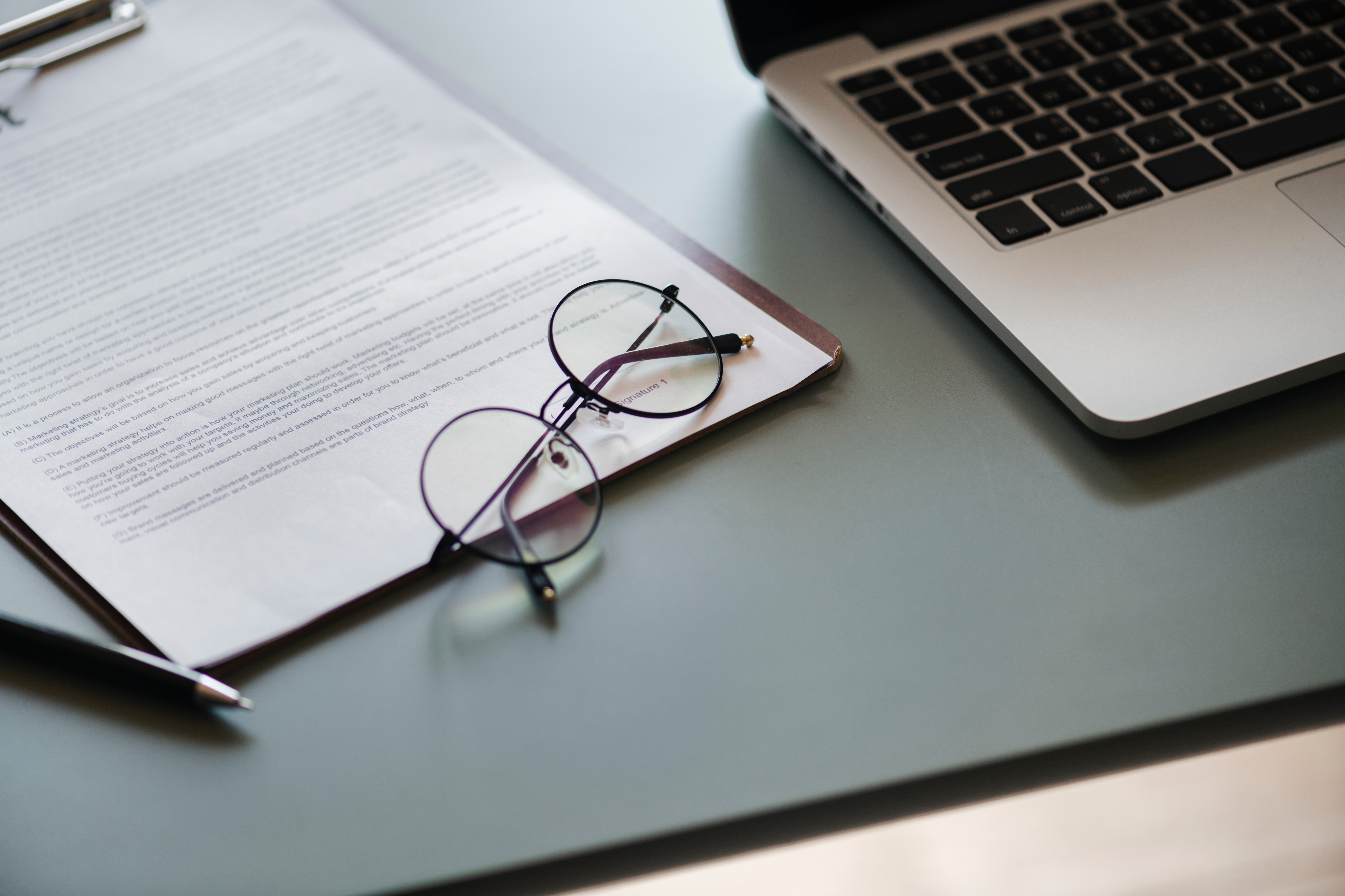 photo of a laptop, a pair of glasses, and a contract on a table